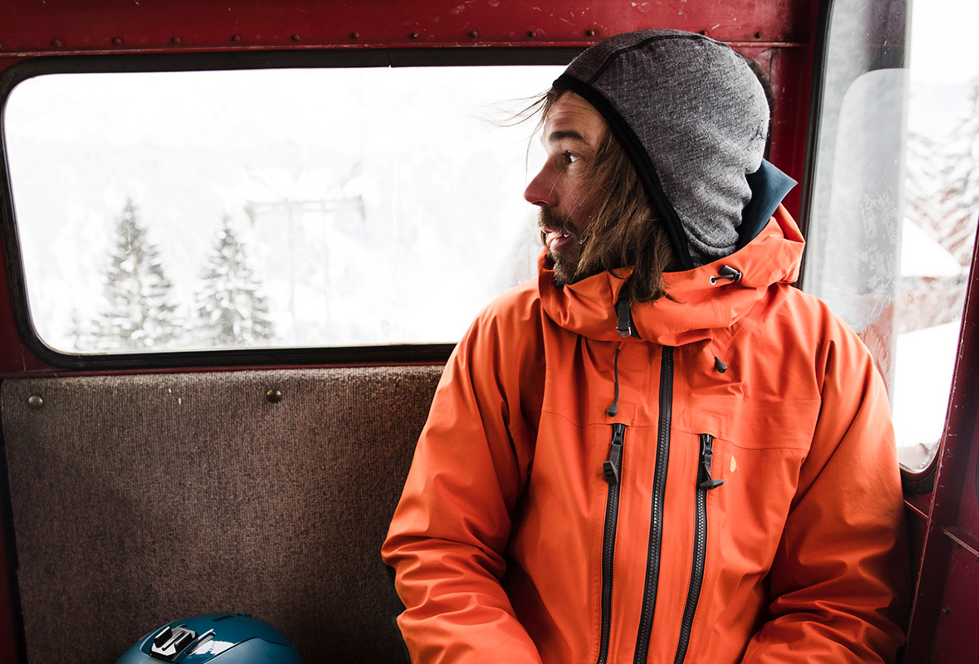Man riding in snowcat looking outside in orange jacket