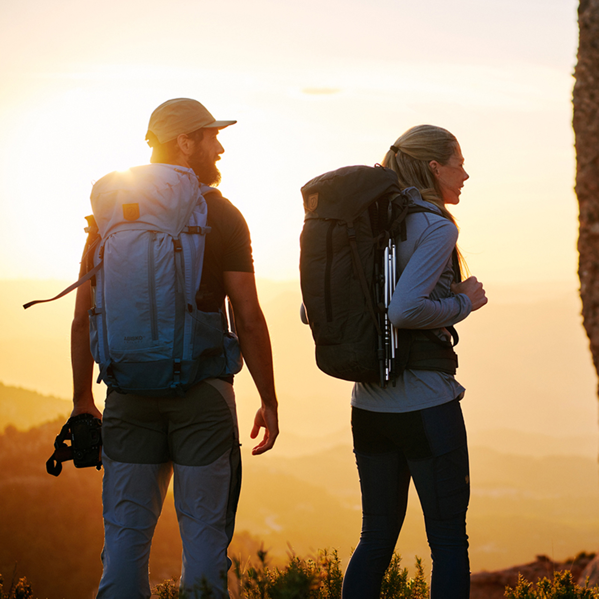 Two people walking with large backpacks towards sunset