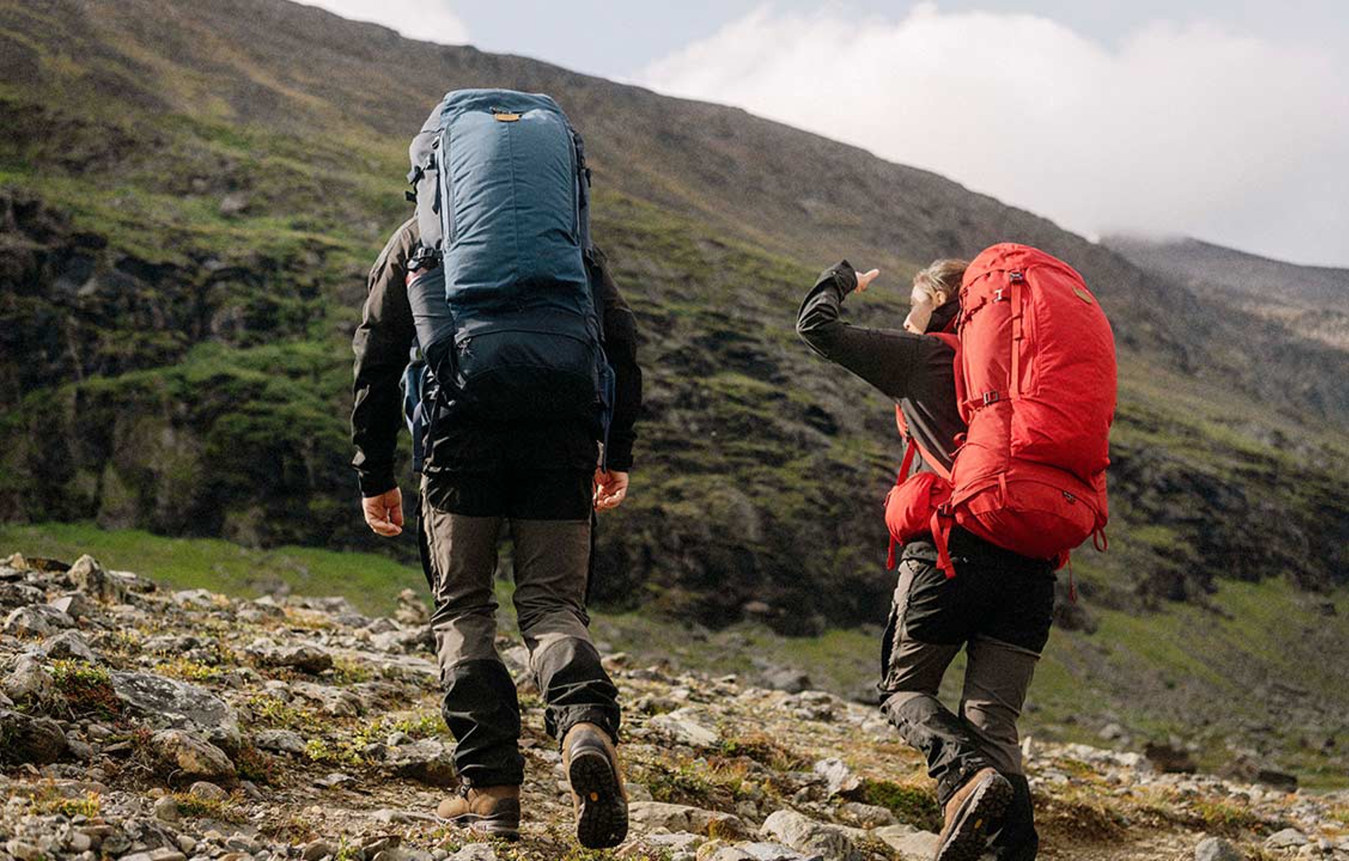 a man and a woman wearing fjallraven apparel trekking up a mountain together