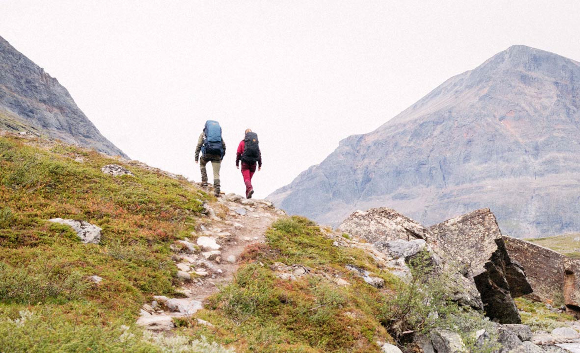 two people trekking on the side of a mountain in Fjallraven apparel and packs