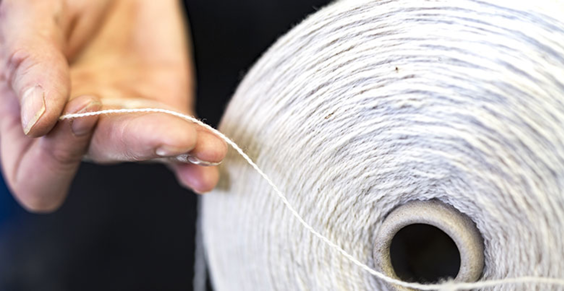 image of a woman holding a thread from a large spool of wool