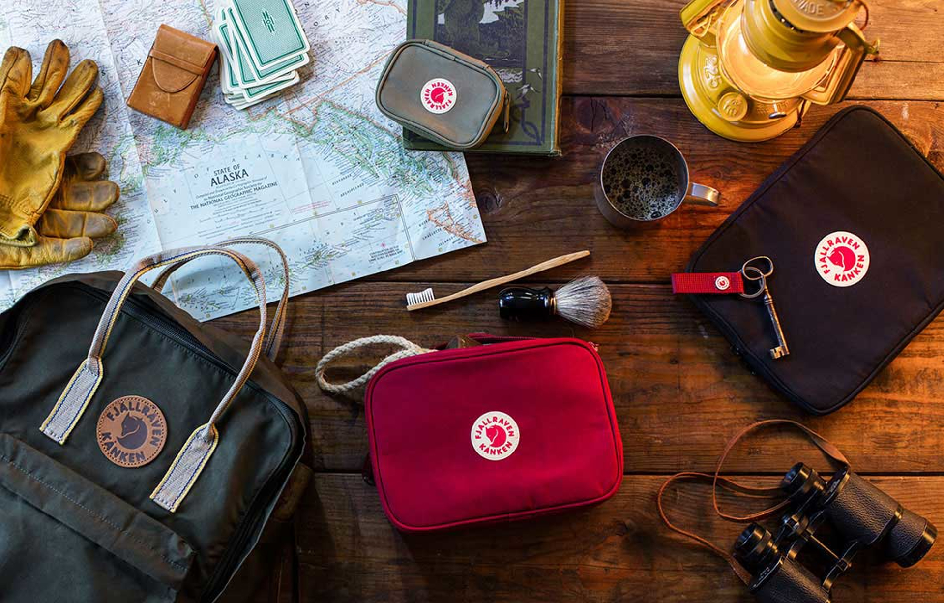 fjallraven kanken accessory bags with shaving brush, tooth brush, key, mug, lantern,  a book and a map on a table