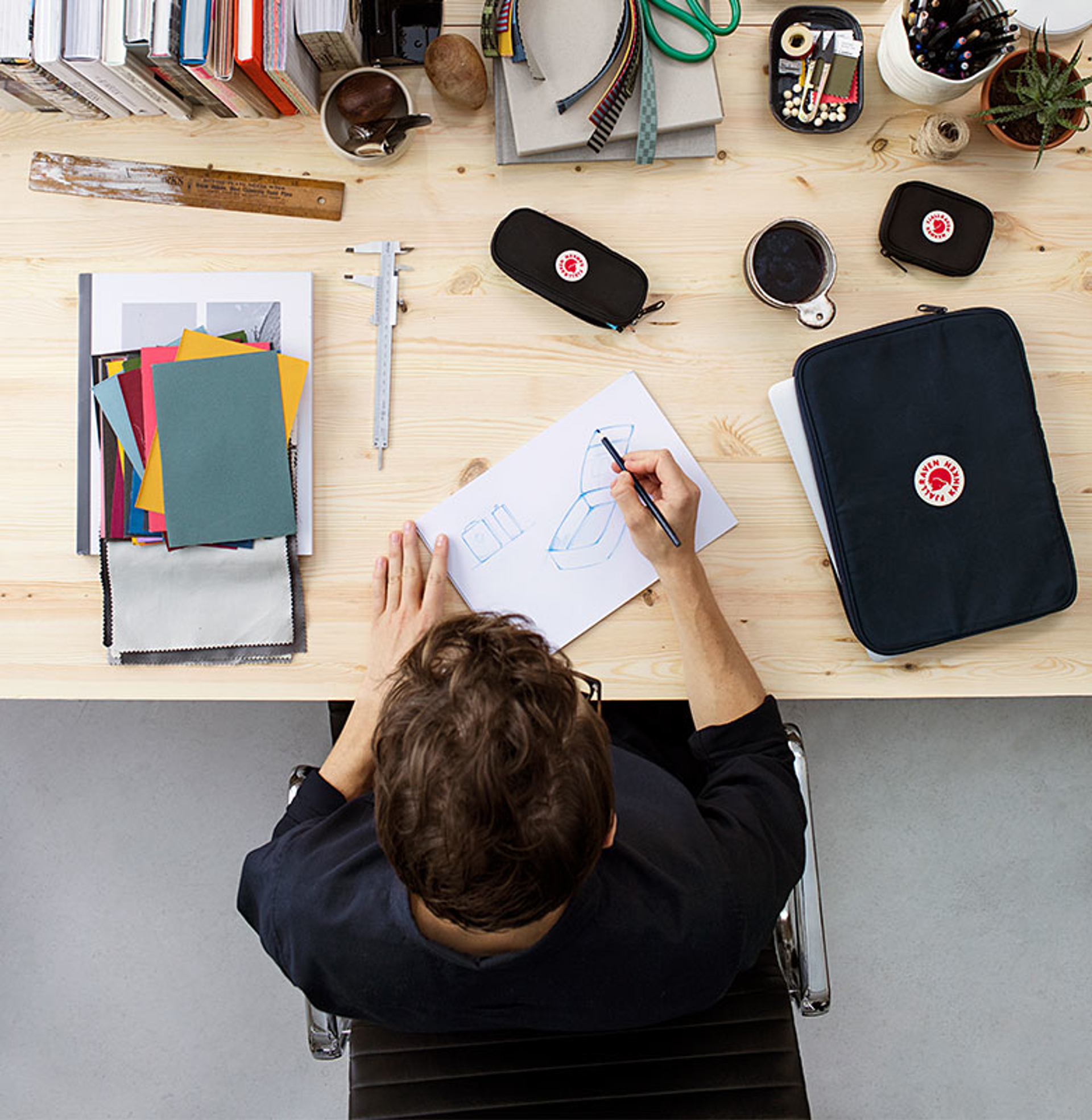 man sitting a workstation with fjallraven gear around him while he sketches