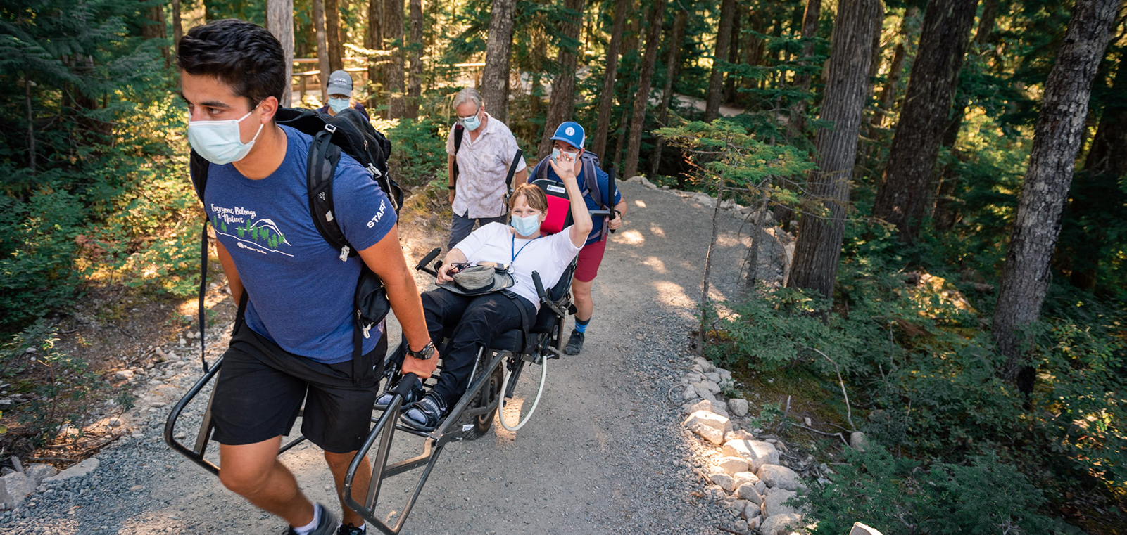 Group helping an off road wheelchair through a forest trail for adaptive recreation. 